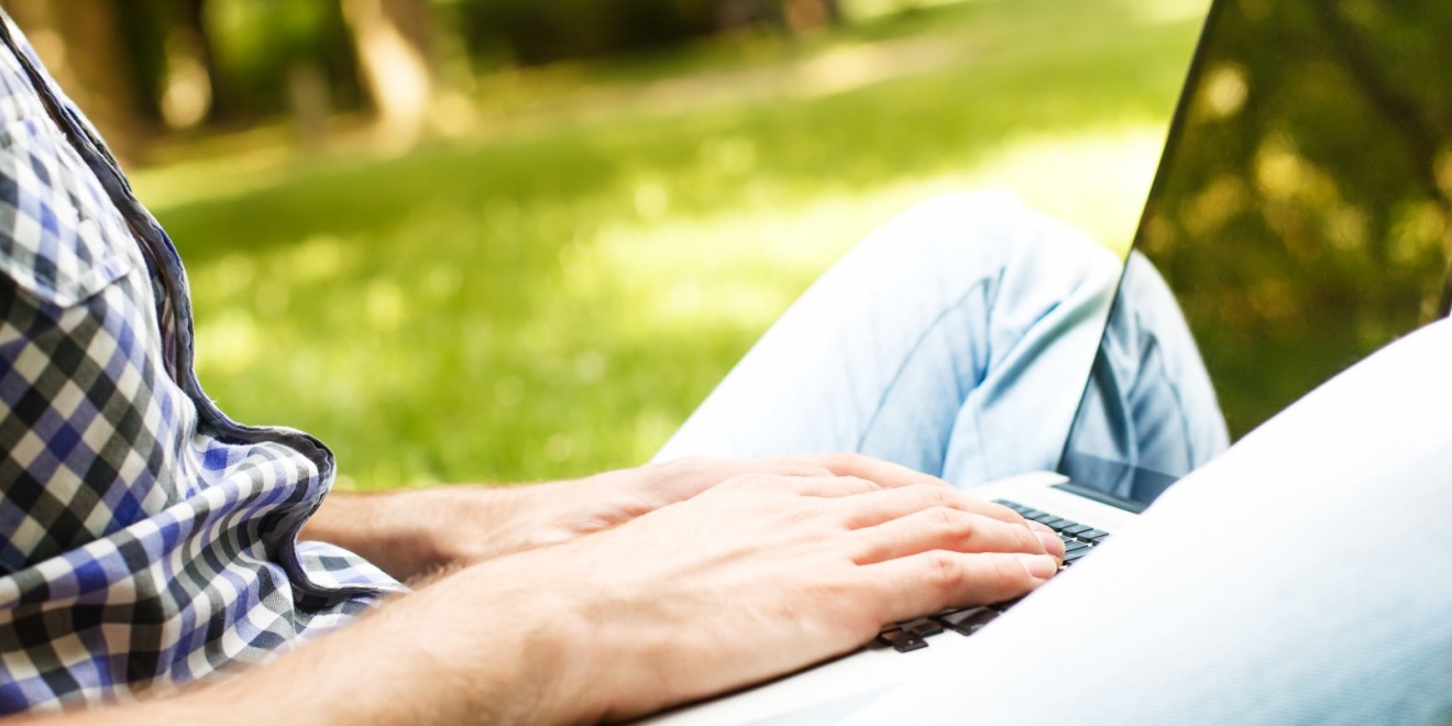 Photo d'une personne assise en tailleur dans l'herbe tapant sur un ordinateur