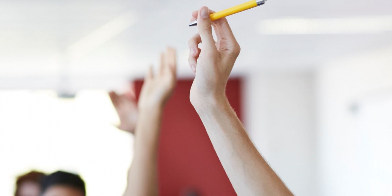 Gros plan de mains levées avec un stylo dans une classe