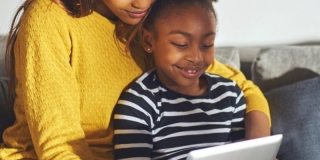 Photographie d'une femme avec une petite fille sur les genoux les deux regardant des contenus sur une tablette