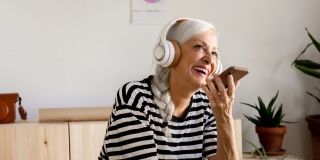 Photographie d'une femme aux cheveux blancs natée au téléphone avec un casque sur les oreilles assise en intérieur