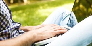 Photo d'une personne assise en tailleur dans l'herbe tapant sur un ordinateur