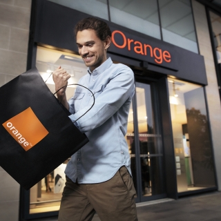 Homme qui sort d'une boutique Orange avec un sac aux couleurs d'Orange