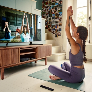 Jeune femme suivant un cours de yoga dans son salon face à la TV
